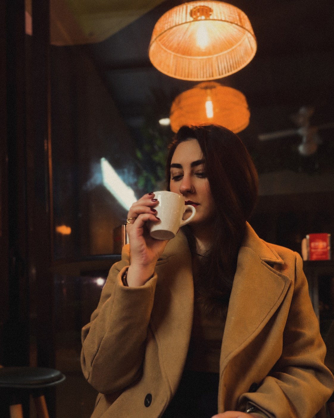 Rachel Cossich, de casaco, tomando café sob luminárias acesas num café à noite